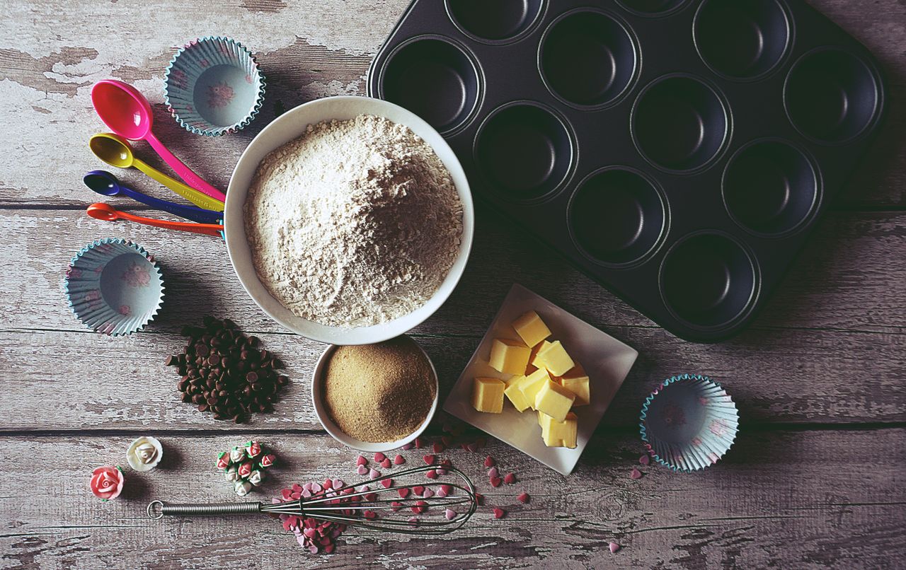 Services Flat lay of baking ingredients and tools for making cupcakes, including flour, butter, and chocolate chips.