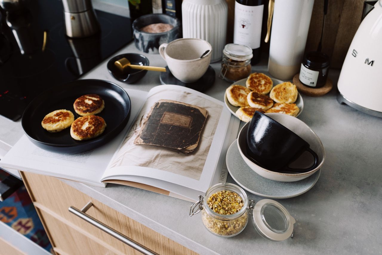 Services High angle of cookbook and cooked fritters on plates placed on table near utensils and ingredients in cozy kitchen at home