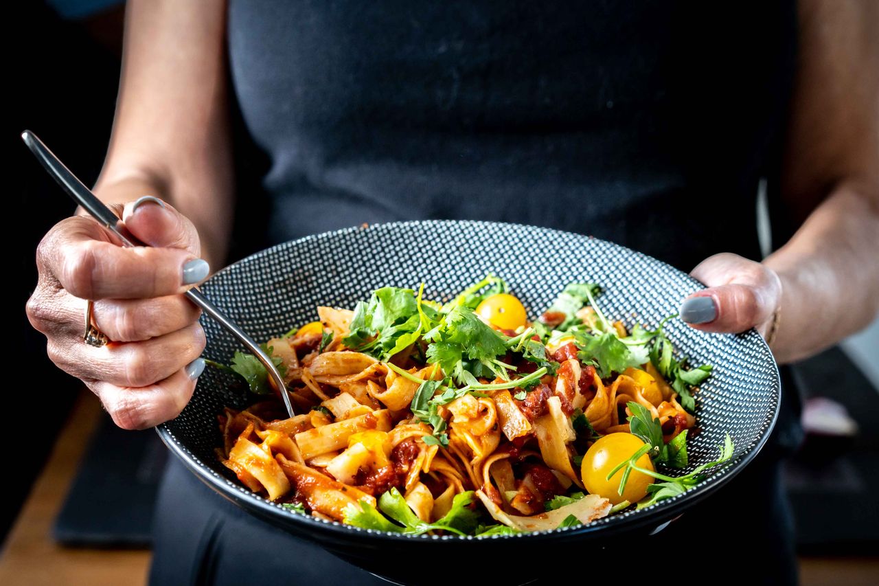 Services Close-up of woman holding a bowl of fresh pasta garnished with cilantro and cherry tomatoes.